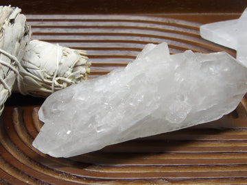 Large semi-polished clear quartz point with natural inclusions on wooden display