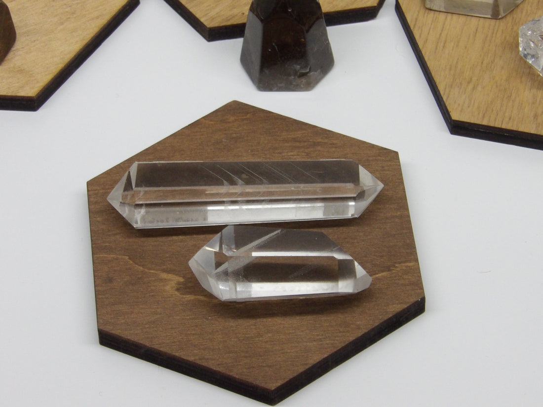 Two polished double-terminated phantom quartz points on a wooden display, 2 and 3 inches in size.