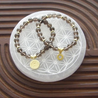 Smoky quartz bracelet featuring 18k gold-plated lotus charm and gold spacers; sun charm shown is gold-tone.